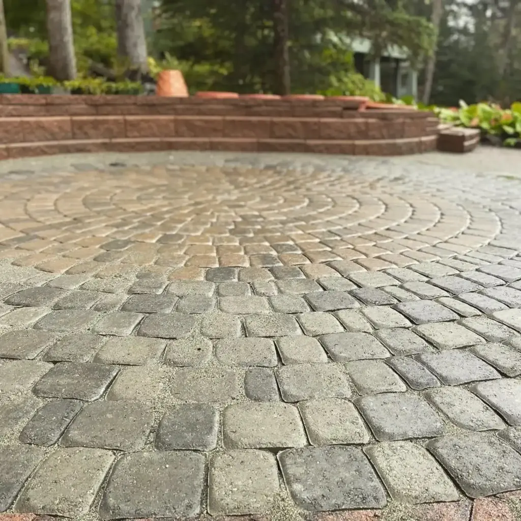 Circular cobblestone paver patio with a raised brick seating wall behind it