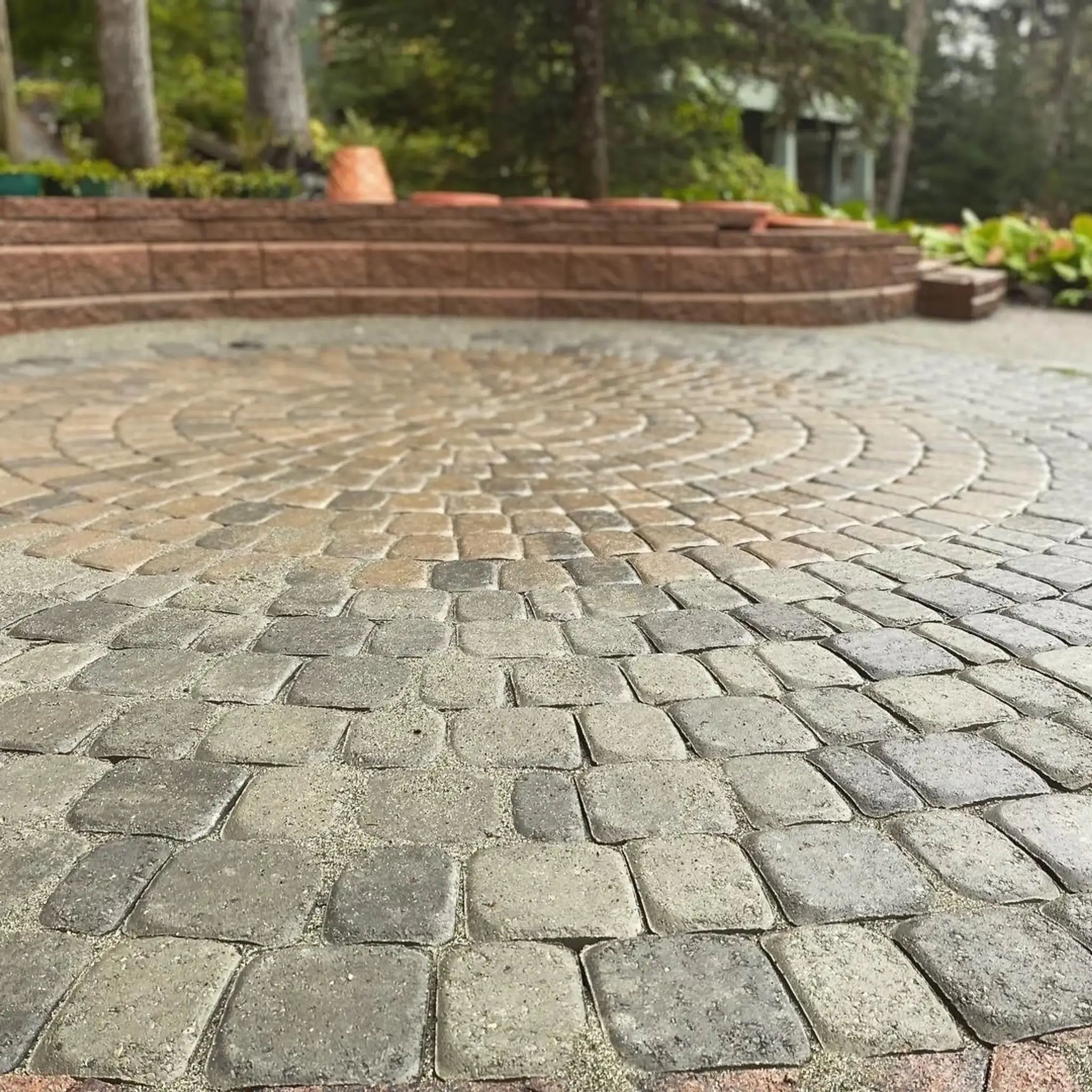 Circular cobblestone paver patio with a raised brick seating wall behind it