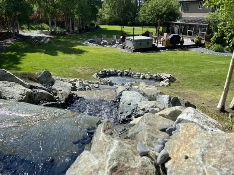 Boulder-lined stream running through a lawn towards a covered seating area