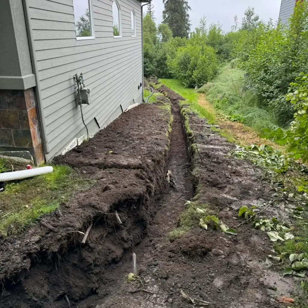 Drainage trench dug along a house foundation with pipe ready to be laid