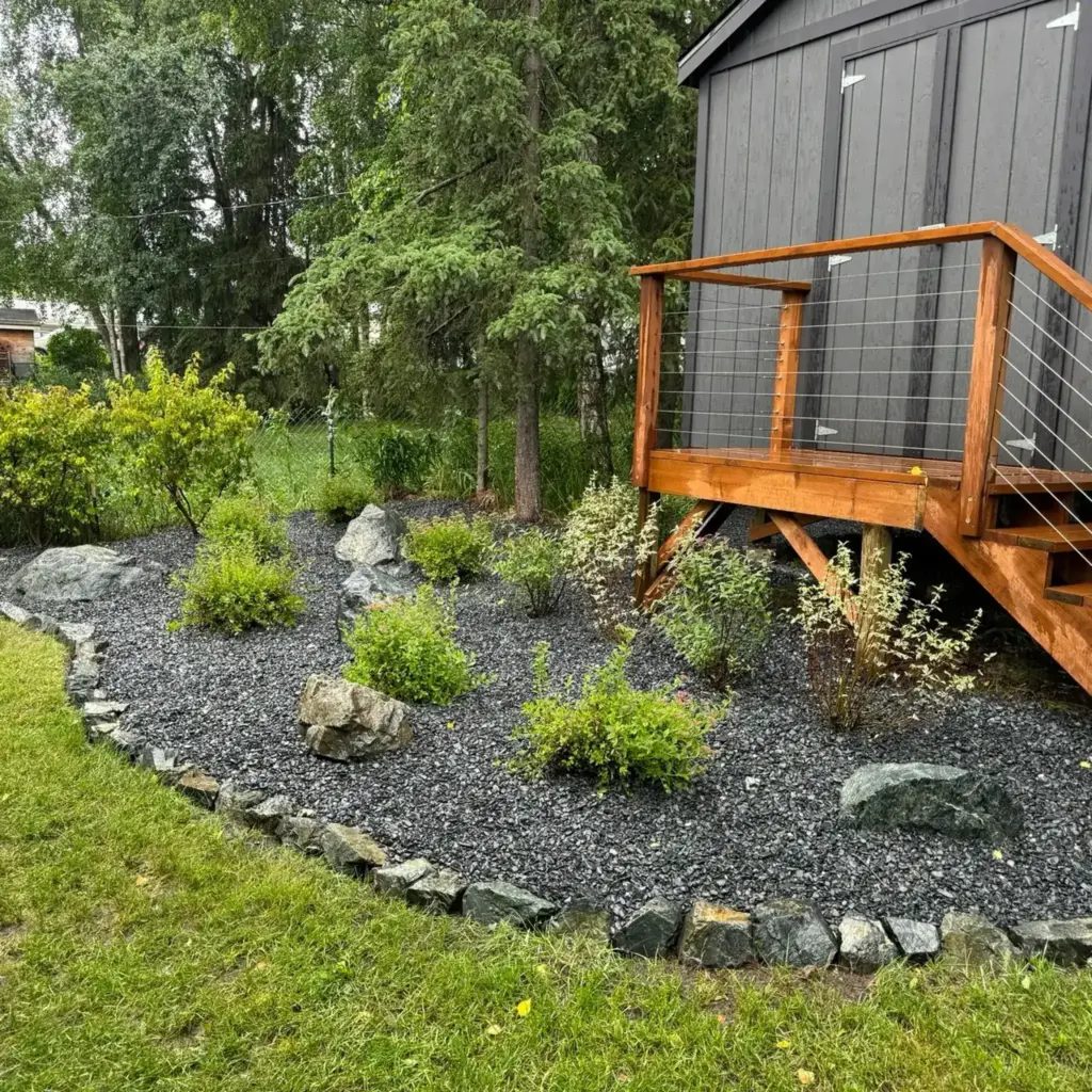 Curved planting bed of shrubs set in black rock mulch beside a cedar deck