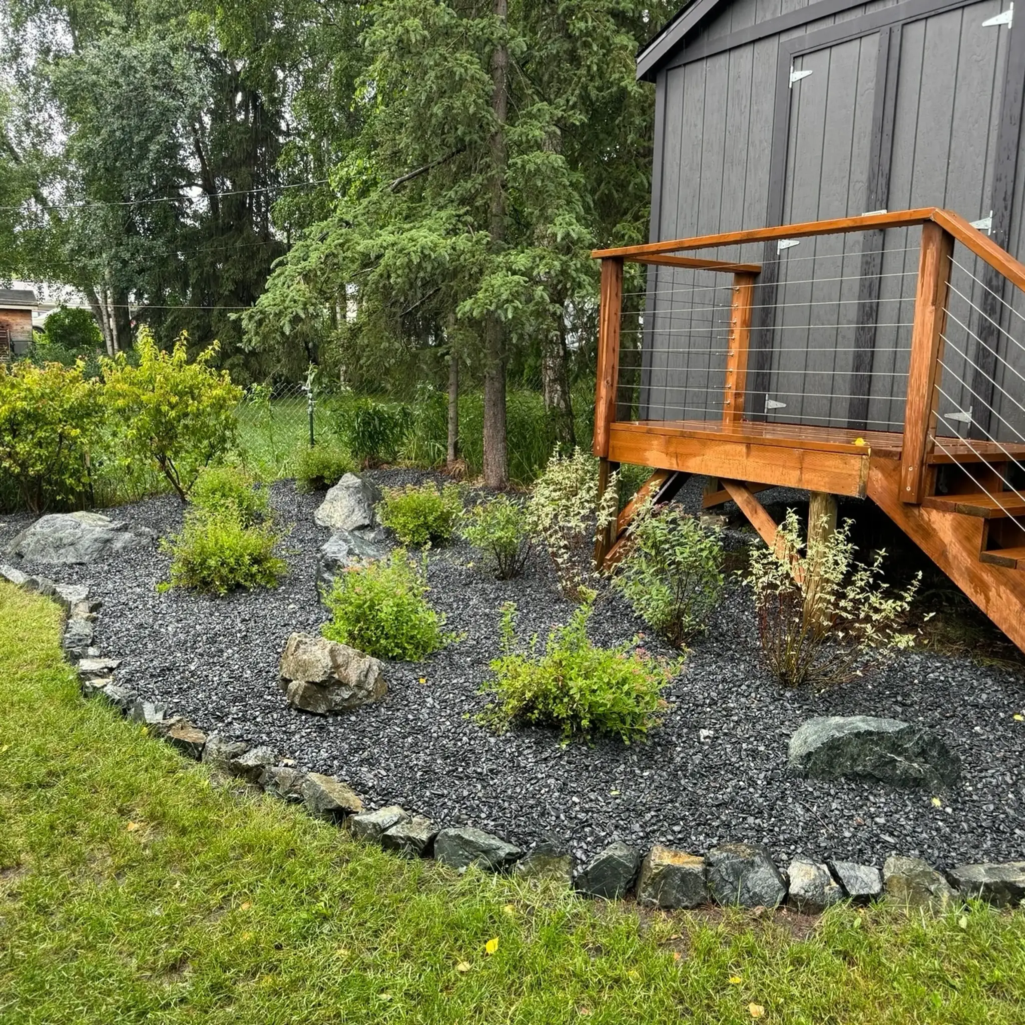 Curved planting bed of shrubs set in black rock mulch beside a cedar deck