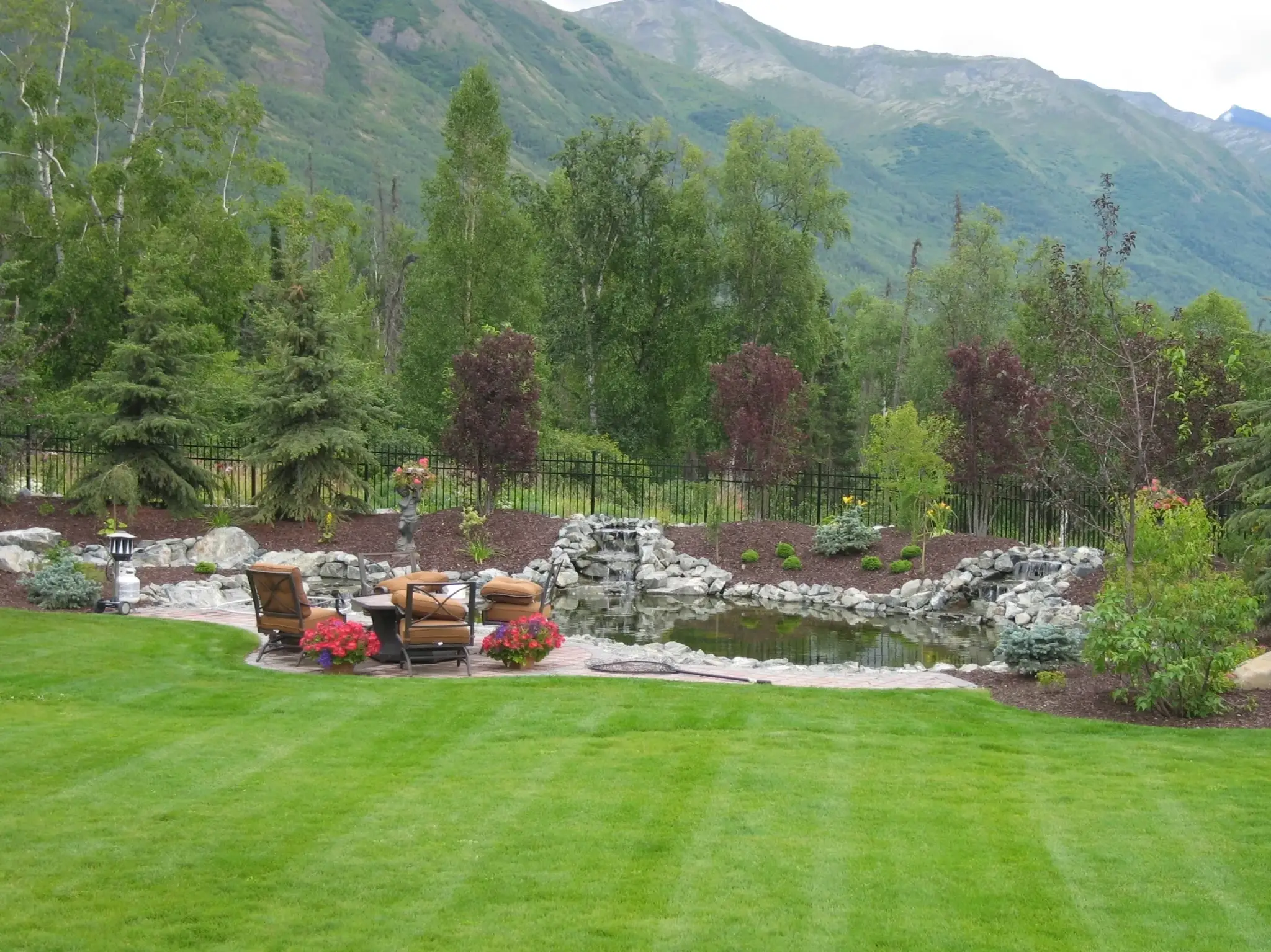 Striped lawn leading to a rock waterfall, pond and patio with mountain views
