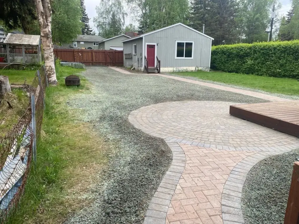 Curved paver walkway sweeping across a gravel driveway towards a house