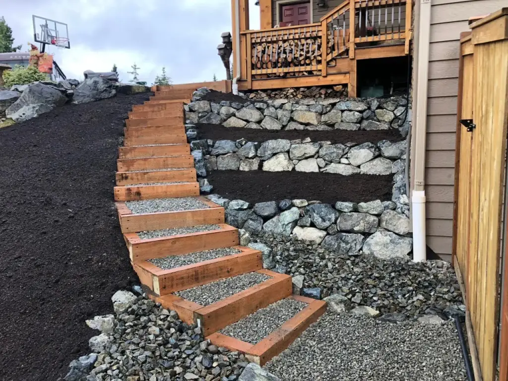 Timber steps set into a boulder retaining wall above dark mulch beds